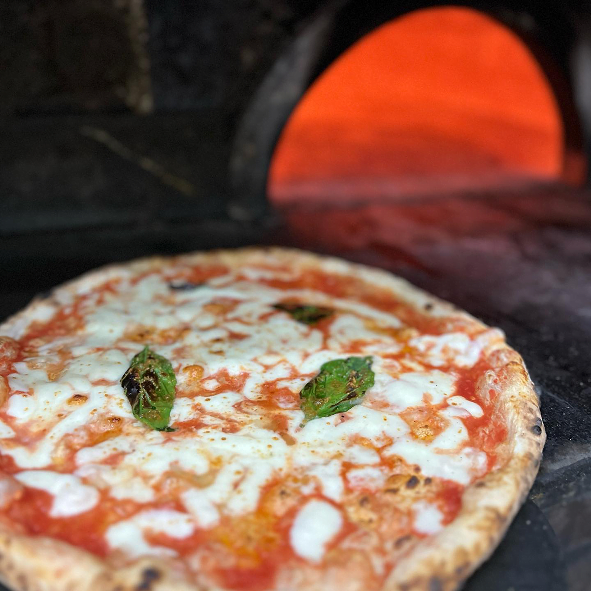 Pizza napoletana with a wood burning oven in the background