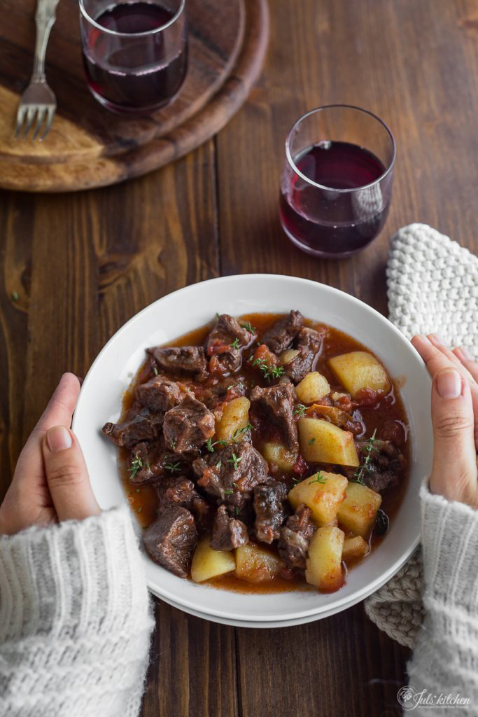 Spezzatino (Italian beef stew) in a white bowl with a glass of red wine to the side